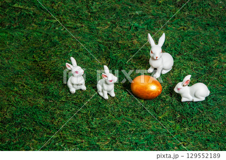 Little white bunnies around golden egg on a background of moss. Little white bunnies around golden egg on a background of moss. 129552189