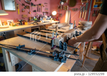 Builder hands press wooden pieces with clamps after apply adhesive for sturdy board. Surface smooth 129552299