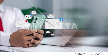 Email, contact, online communication, messaging, and business correspondence in a modern office. Close-up of businessman holding smartphone with digital email icons and notifications. 129552388