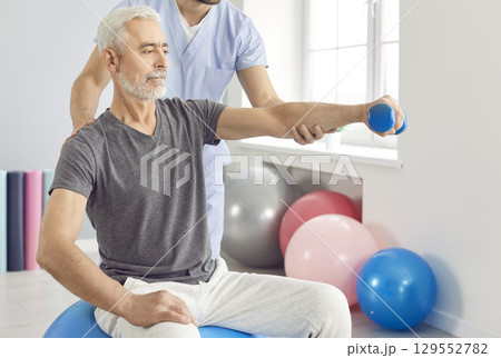Physician or physiotherapist helping patient to do exercises with dumbbel during arm rehabilitation. Physician or physiotherapist helping patient to do exercises with dumbbel during arm rehabilitation. 129552782