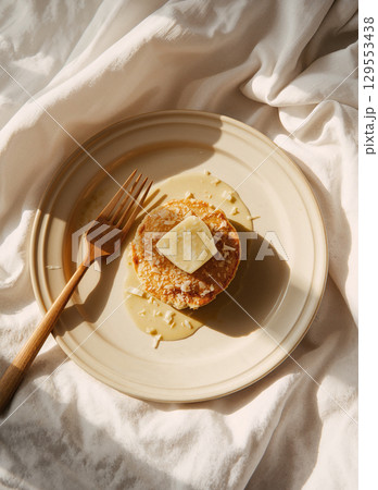 A single golden pancake topped with a square of melting butter, sweet syrup, and a sprinkle of coconut, creating a simple yet delicious homemade breakfast. 129553438