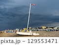 Windsock Stormy sky over sandy beach in summer. Catamaran sun loungers and umbrellas. Empty coastline 129553471