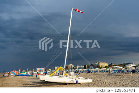 Windsock Stormy sky over sandy beach in summer. Catamaran sun loungers and umbrellas. Empty coastline 129553471
