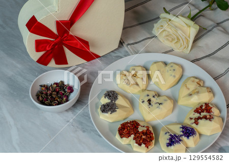 Heart-shaped chocolates with floral decoration on marble table with rose and gift box 129554582