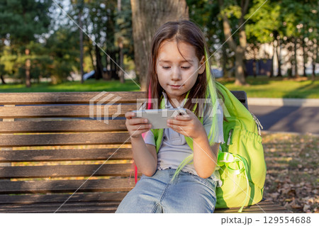 Young girl engaged with smartphone sitting on park bench 129554688