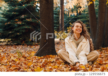 Smiling young woman sits in the autumn foliage on the ground of the forest with the yellow leaves 129556673