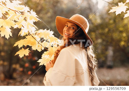 Smiling young woman portrait in the autumn forest with the yellow leaves at sunset 129556709