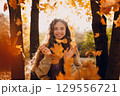 Smiling young woman throws up the yellow autumn leaves in the forest at sunset 129556721