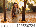 Smiling young woman walking in autumn forest with the yellow leaves at sunset 129556726