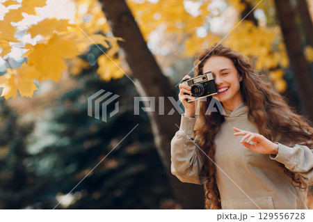 Smiling young woman photographer with the photo camera shooting the forest trees with the yellow leaves at sunset 129556728