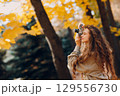 Smiling young woman with the photo camera shooting the forest trees with the yellow leaves at sunset 129556730