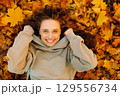 Smiling young woman lies on the autumn foliage in the park with the yellow leaves 129556734