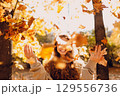 Smiling young woman throw up the autumn leaves in the forest at sunset 129556736