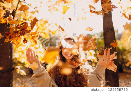 Smiling young woman throw up the autumn leaves in the forest at sunset 129556736