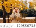 Smiling young woman with curly hairstyle enjoys the autumn weather in the forest with the yellow leaves at sunset 129556738