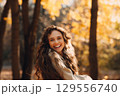 Smiling young woman enjoying the autumn season in the fall park with the yellow leaves at sunset 129556740