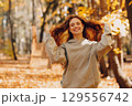 Smiling young woman with curly hairstyle enjoys the autumn weather in the forest with the yellow leaves at sunset 129556742