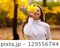 Young woman holds yellow leaf in her hand with smile in the park at sunset 129556744