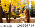 Smiling young woman touching the autumn leaves on maple tree in the forest 129556746