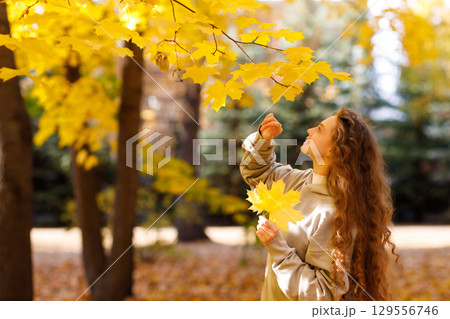 Smiling young woman touching the autumn leaves on maple tree in the forest 129556746