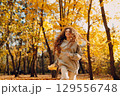 Smiling young woman plays and jumping dancing in the autumn park with the yellow leaves at sunset 129556748