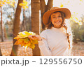 Smiling young woman in the autumn forest with the yellow leaves with sunset rays 129556750