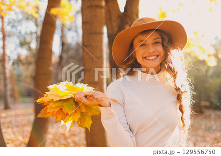 Smiling young woman in the autumn forest with the yellow leaves with sunset rays 129556750