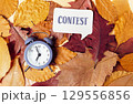 Clock is on top of a pile of leaves with the word Contest written in a speech 129556856