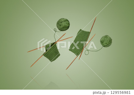 Green knitted wool with knitting needles for knitting warm clothes and hobbies needlework flying in air on green background Green knitted wool with knitting needles for knitting warm clothes and hobbies needlework flying in air on green background 129556981