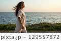 Woman enjoying a serene walk by the ocean at sunset 129557872