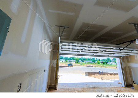 Newly constructed garage interior with drywall open door revealing construction site outside Newly constructed garage interior with drywall open door revealing construction site outside 129558179