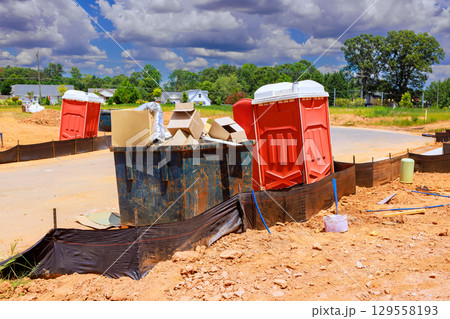 Construction site with portable toilets, debris under bright blue sky during works day Construction site with portable toilets, debris under bright blue sky during works day 129558193