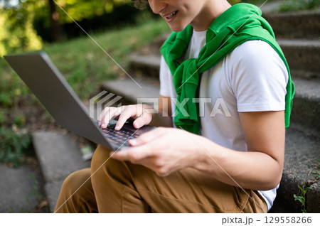 Teen sitting on the steps in the park and working on laptop Teen sitting on the steps in the park and working on laptop 129558266