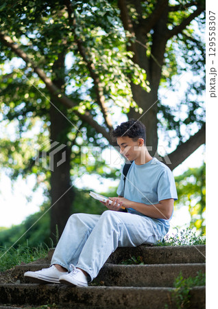 Dark-haired positive teen sitting on the steps in the park Dark-haired positive teen sitting on the steps in the park 129558307