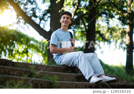 Dark-haired positive teen sitting on the steps in the park 129558310