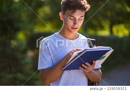 Dark-haired teen with a book in the park looking interested and contented 129558321