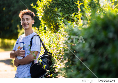 Dark-haired teen looking confident and smiling while standing in the park 129558324