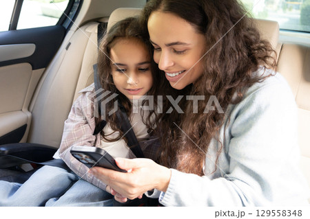 Mom and daughter spending time together and watching something while sitting in a car 129558348