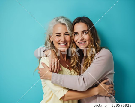 Two women smiling and embracing against a bright blue background during a joyful moment 129559925