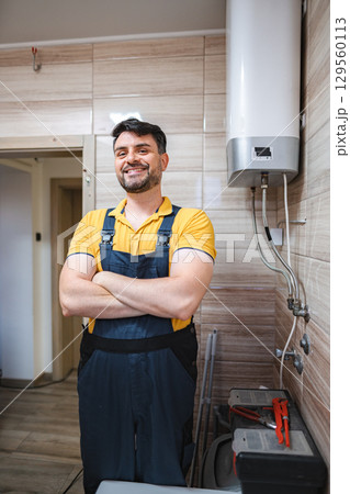 Plumber smiling with arms crossed next to water heater in bathroom Plumber smiling with arms crossed next to water heater in bathroom 129560113