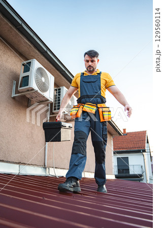 Technician walking on roof while carrying toolbox and inspecting air conditioning units Technician walking on roof while carrying toolbox and inspecting air conditioning units 129560114