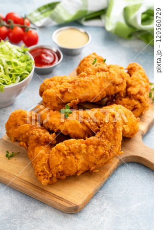 Chicken tenders served on a wooden board with salad and sauces 129560729