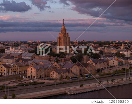 The Latvian Academy of Sciences stands at the center, surrounded by historic buildings. A waterfront area and soft pink and purple skies complete the scene. 129560890