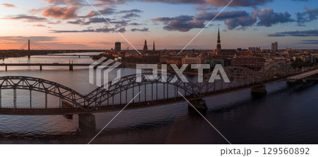 Riga, Latvia at sunset featuring the Daugava River, Railway Bridge, Riga TV Tower, Vansu Bridge, and spires of St. Peter's Church in the old town. 129560892