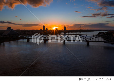 Sunset view of Riga, Latvia, featuring the arched railway bridge over the Daugava River, the National Library, and the Riga TV Tower in the distance. 129560903