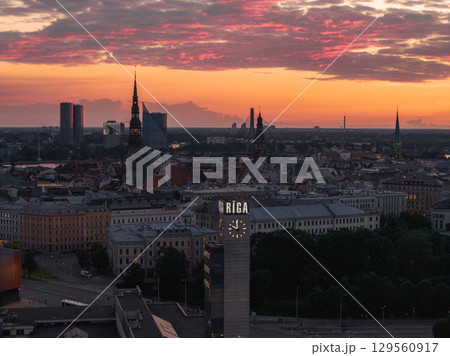 Riga's old town spires, including St. Peter's Church and Riga Cathedral, stand against a vibrant orange and pink sunset, with a clock tower in the foreground. Riga's old town spires, including St. Peter's Church and Riga Cathedral, stand against a vibrant orange and pink sunset, with a clock tower in the foreground. 129560917
