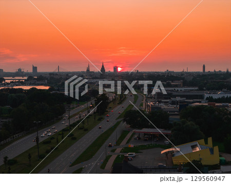 A sunset view of Riga, Latvia, featuring the old town spires, Riga TV Tower, Daugava River, a bridge, and a tree lined road with vehicles. A sunset view of Riga, Latvia, featuring the old town spires, Riga TV Tower, Daugava River, a bridge, and a tree lined road with vehicles. 129560947