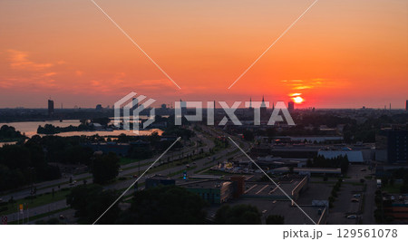 Warm sunset over Riga, Latvia, featuring the Riga TV Tower, old town spires, Daugava River, a bridge, urban roads, buildings, and greenery. 129561078