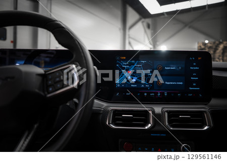 Close up of a vehicle's dashboard featuring a digital display with a navigation map in Russian, metallic air vents, and a sleek steering wheel design. 129561146