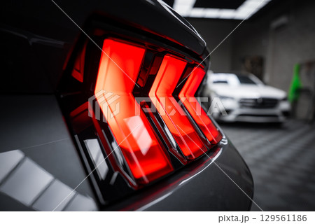 Rear taillight of Ford Mustang GT 5.0 with tri bar LED design illuminated. A white Mercedes AMG G Class is visible in a modern showroom setting. Rear taillight of Ford Mustang GT 5.0 with tri bar LED design illuminated. A white Mercedes AMG G Class is visible in a modern showroom setting. 129561186